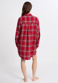 Czerwona koszula flanelowa w kratę, z długimi rękawami, zapięciem na guziki przy mankietach, z zaokrąglonym dołem, z pionowymi i poziomymi liniami w czerni i bieli na całej powierzchni.