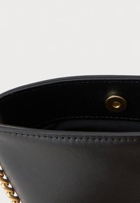 Interno di una borsa in pelle nera che mostra una texture liscia, una chiusura a pulsante dorato e un accento di catena lungo il lato.