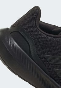 Černá sportovní bota s texturovaným pleteným svrškem, hladkou gumovou podrážkou a štíhlým designem s jemnými akcenty brandingu.