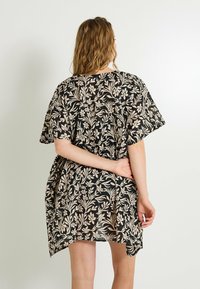 Vestido negro con estampado floral en tonos beiges, de mangas cortas, corte relajado y bajo asimétrico. Tela ligera y fluida.