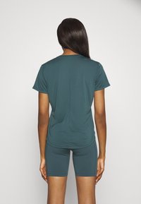 Top atlético en color azul verdoso con mangas cortas y un diseño ligeramente ajustado, combinado con pantalones cortos tipo biker a juego, ambos en una suave tela elástica.