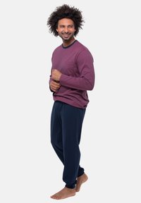 Donkerrode longsleeve shirt met een textuurpatroon en een borstzak, gecombineerd met marineblauwe broek van zacht materiaal, op blote voeten gedragen.