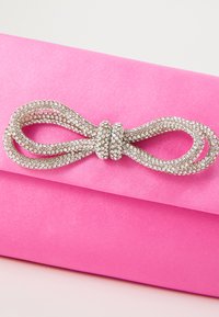 Busta di satin rosa con un accento di fiocco argento scintillante, caratterizzata da un design attorcigliato e dettagli in strass in una finitura liscia e lucida.
