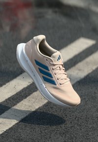 Hellrosa Sportschuh mit blauen Streifen, strukturiertem Stoffobermaterial, gepolsterter weißer Sohle, mit Schnürsenkeln und abgerundetem Zehendesign.