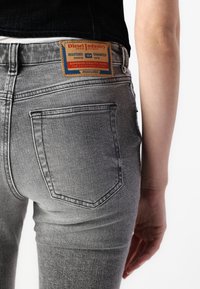 Faded gray denim jeans with a fitted design, featuring a prominent brand label and standard back pockets with double stitching.