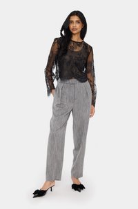 Fekete csipkeborítású, hosszú ujjú felső virágmintával, szürke csíkos, magas derekú nadrággal és fekete, masnis, hegyes orrú magassarkú cipővel párosítva.