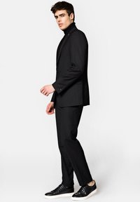 Czarny garnitur o dopasowanym kroju, połączony z czarnym golfem i czarnymi sneakersami o fakturowanej powierzchni. Charakteryzuje się gładkimi liniami i dopasowaną sylwetką.