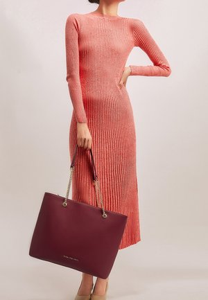 Robe en tricot côtelé corail à manches longues, accompagnée d'un sac fourre-tout en cuir bourgogne avec des chaînes en or et une texture lisse.