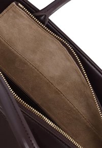 Interno di una borsa in pelle marrone con una morbida fodera in suede color beige, dotata di una cerniera dorata e una texture liscia. Nessun logo o motivo visibile.