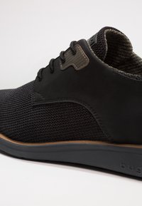 Sneaker nera con tomaia in maglia texturizzata, dettagli in pelle e suola in gomma grigia. Presenta chiusura con lacci e supporto per la caviglia imbottito.