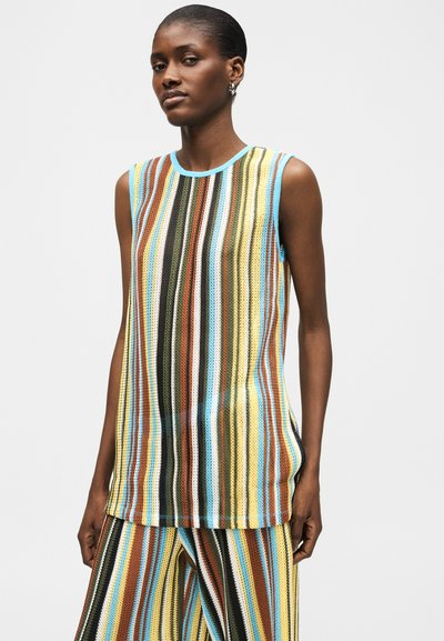 Γυναίκα που φοράει αμάνικο πλεκτό τοπ και παντελόνι με κάθετες πολύχρωμες ρίγες σε καφέ, κίτρινο, μπλε, μαύρο και άσπρο.