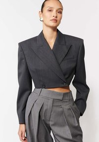 Szary skórzany żakiet w stylu cropped z podwójnym zapięciem, strukturalnymi ramionami i czarnymi guzikami, połączony z szarymi spodniami w paski z wysokim stanem.