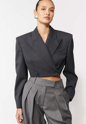 Szary skórzany żakiet w stylu cropped z podwójnym zapięciem, strukturalnymi ramionami i czarnymi guzikami, połączony z szarymi spodniami w paski z wysokim stanem.