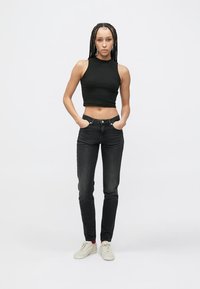 Fekete crop top, sötét farmers nadrág és fehér tornacipő. A szett testhezálló szabású és sima textúrájú. Egyszerű háttér.