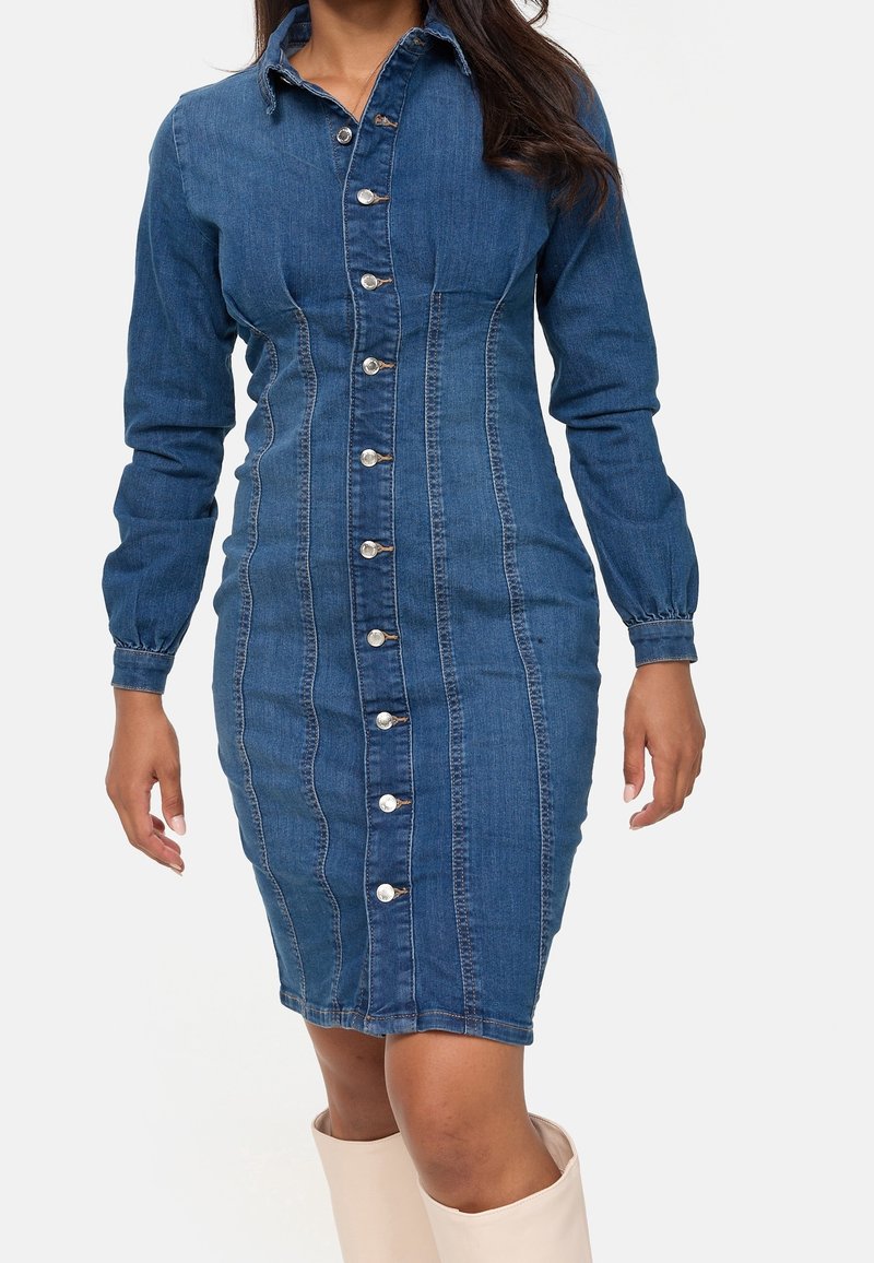 Femme portant une robe en jean bleu ajustée à manches longues boutonnée, associée à des bottes montantes de couleur claire.