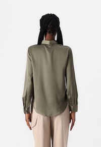 Camisa de satén verde oliva con mangas largas y dobladillo redondeado, que presenta un cuello clásico y puños abotonados, mostrada desde la parte de atrás.