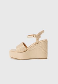 Sandales compensées beiges avec une plateforme texturée, dotées d'une sangle lisse et d'une boucle à la cheville. Motif complexe sur le côté de la semelle compensée.