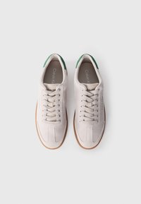 Baskets gris clair avec une texture en daim, bout rond, lacets blancs, accents de talon verts et semelle en gomme. Marque Calvin Klein sur le côté.