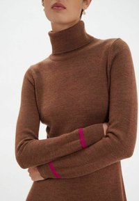Pull à col roulé marron en tissu tricoté doux, avec des accents roses sur les poignets. Design ajusté avec des manches longues.