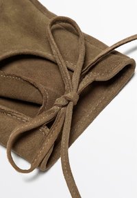 Brun ruskinds pouch med en bundet lukning. Den har en blød tekstur, syninger i detaljerne og en rund form. Overfladen fremstår glat og mat.