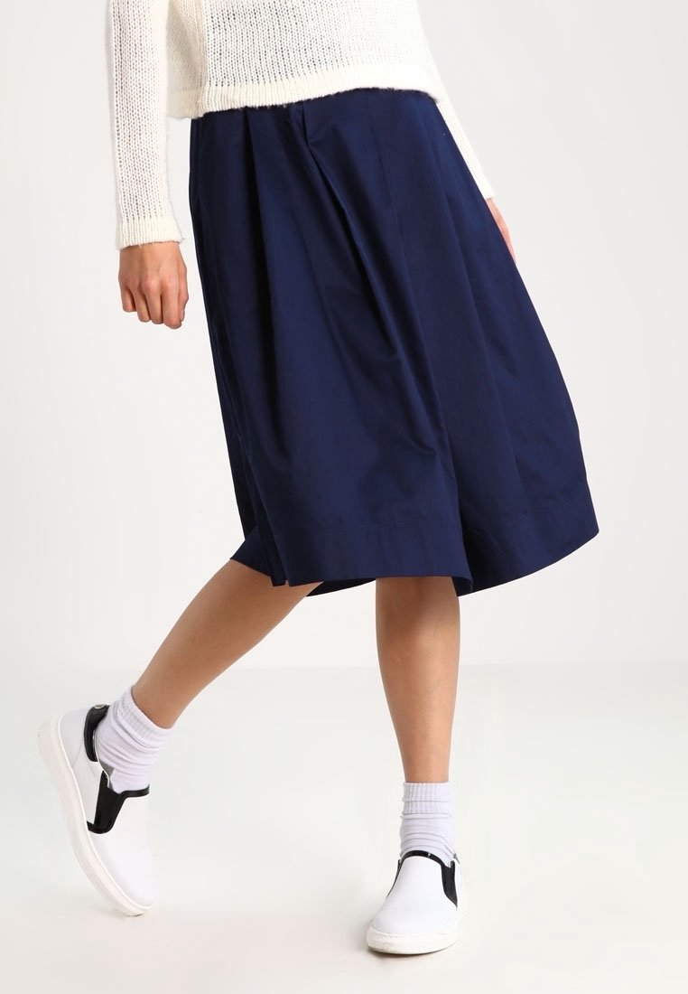 Gonna midi plissettata blu navy realizzata in tessuto leggero, con una texture liscia e una vestibilità comoda, abbinata a scarpe bianche slip-on.
