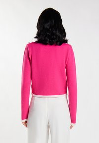 Maglione rosa corto con maniche lunghe, tessuto a trama e bordo bianco a contrasto all'orlo e ai polsini. Bottoni decorativi dorati sulle spalle.