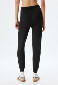 Schwarze sportliche Jogginghosen mit schmalem Schnitt, elastischem Bund, seitlichen Taschen und gerippten Bündchen. Das Material sieht glatt und dehnbar aus.