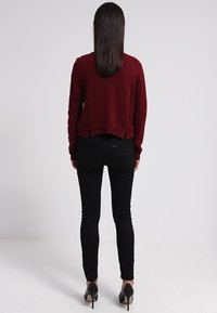 Burgundská pletená svetr s cropped designem, s texturovaným vzorem, v kombinaci s černými skinny džínami a černými špičatými podpatky.