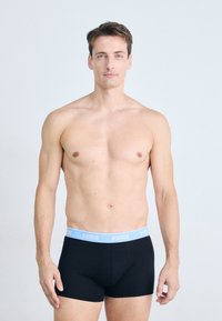 Schwarze Boxerbriefs mit einem hellblauen elastischen Bund, versehen mit dem Logo "PUMA." Model steht in neutraler Pose vor einem schlichten Hintergrund.