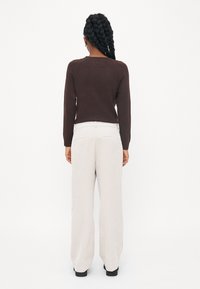 Pull marron à manches longues et décolleté rond, associé �à un pantalon large gris clair, avec une finition texturée et des poches arrière.