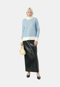 Pullover maglione a costine di colore blu chiaro con un colletto bianco, abbinato a una maxi gonna in pelle nera. La modella tiene una borsa di colore crema. Scarpe nere.
