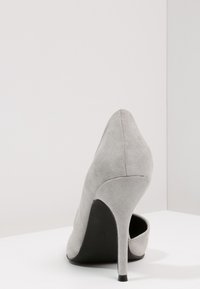 Scarpa con tacco alto in suede grigio con punta affusolata e sottile tacco nero. Il design presenta una superficie liscia e un'apertura sul tallone.