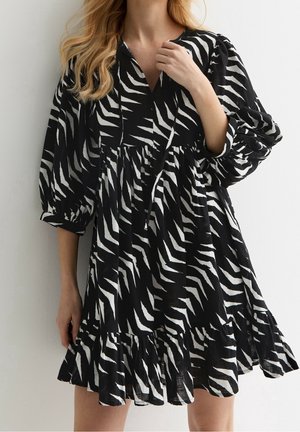 Robe imprimée zèbre en noir et blanc avec des manches longues bouffantes, un décolleté en V et un ourlet à volants. Confectionnée dans un tissu léger.