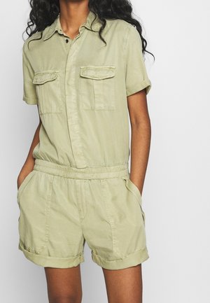 Jumpsuit corto de manga corta en verde claro con cierre de botones en la parte delantera, dos bolsillos en el pecho, cintura elástica y puños enrollados. Textura de tela suave.