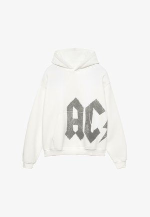 Sweat à capuche blanc avec un grand motif pailleté argenté "AC" et un éclair. Comprend une poche avant et des poignets côtelés. Matériau doux.