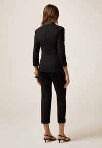 Blazer nero su misura con maniche a tre quarti, abbinato a pantaloni attillati. Taglio slim, orlo risvolto, design minimalista, indossato con tacchi a strappo.