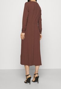 Brązowa ribbed sukienka z długim rękawem, dopasowana w talii, midi długości, o gładkiej teksturze, w zestawieniu z czarnymi sandałami na wysokim obcasie.