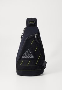 Černá taška na rameno Adidas se zelenými pruhy, síťovanou přední kapsou, stříbrnými zipy a nastavitelným ramenním popruhem na bílém pozadí.