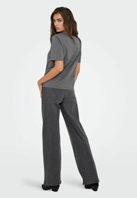 Camiseta gris de manga corta y corte relajado, combinada con jeans grises de pierna ancha. El conjunto presenta un diseño minimalista y una textura suave.