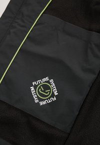 Džep crne jakne sa svijetlozelenim obrubom i okruglim logotipom na kojem piše "Future System" te okružuje stiliziranu ikonu lica.