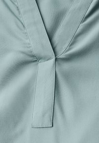 Tissu bleu clair présentant un design en V avec un patte de boutonnage sur le devant, une texture lisse et des détails de couture subtils au niveau du col.