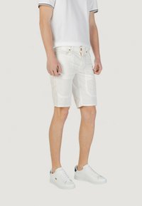 Pantalones cortos blancos con tejido texturizado, bolsillos frontales y cremallera. Combinados con zapatillas blancas con acentos oscuros y cordones.