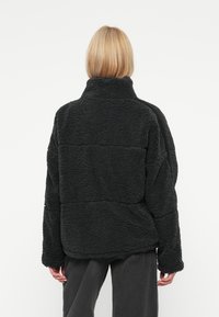 Fleecejacke in Dunkelgrau, mit hohem Kragen, lockerer Passform, strukturiertem Stoff und horizontalen Nähten auf dem Rücken.