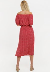 Robe rouge épaules dénudées avec manches courtes bouffantes, taille élastique et motif à pois blancs, longueur mi-mollet, associée à des sandales beiges à talons carrés.