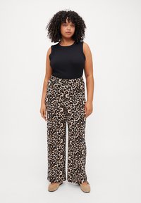 Crna majica bez rukava uparen s širokim hlačama s leopard uzorkom koje imaju bež i crnu shemu boja. Glatka tkanina s opuštenim krojem.
