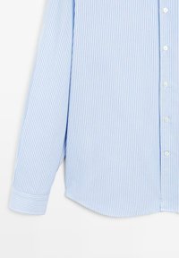 Langarmige blauw-witte shirt met verticale strepen, voorzien van knoopmanchetten en witte knopen aan de voorkant.