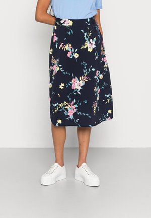 Woman wearing a knee-length dark blue skirt with pink and yellow floral print, light blue top, and white platform sneakers.
