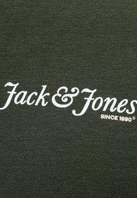 Tmavě zelená látka s texturovaným pletením. Obsahuje název značky "Jack & Jones" v bílé kurzívě, s nápisem "SINCE 1990" pod ním.