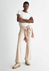 T-shirt bianca con motivo decorativo a catena, pantaloni beige a palazzo legati in vita e stivaletti beige con suola spessa.