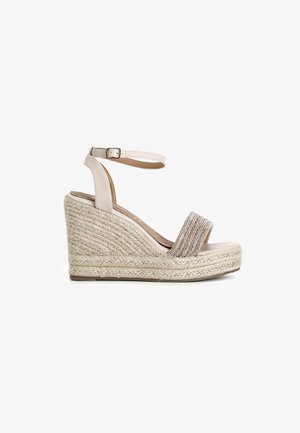 Beige wedge sandal with a rope-textured platform and ankle strap. Features a wide fabric band adorned with shimmering accents.